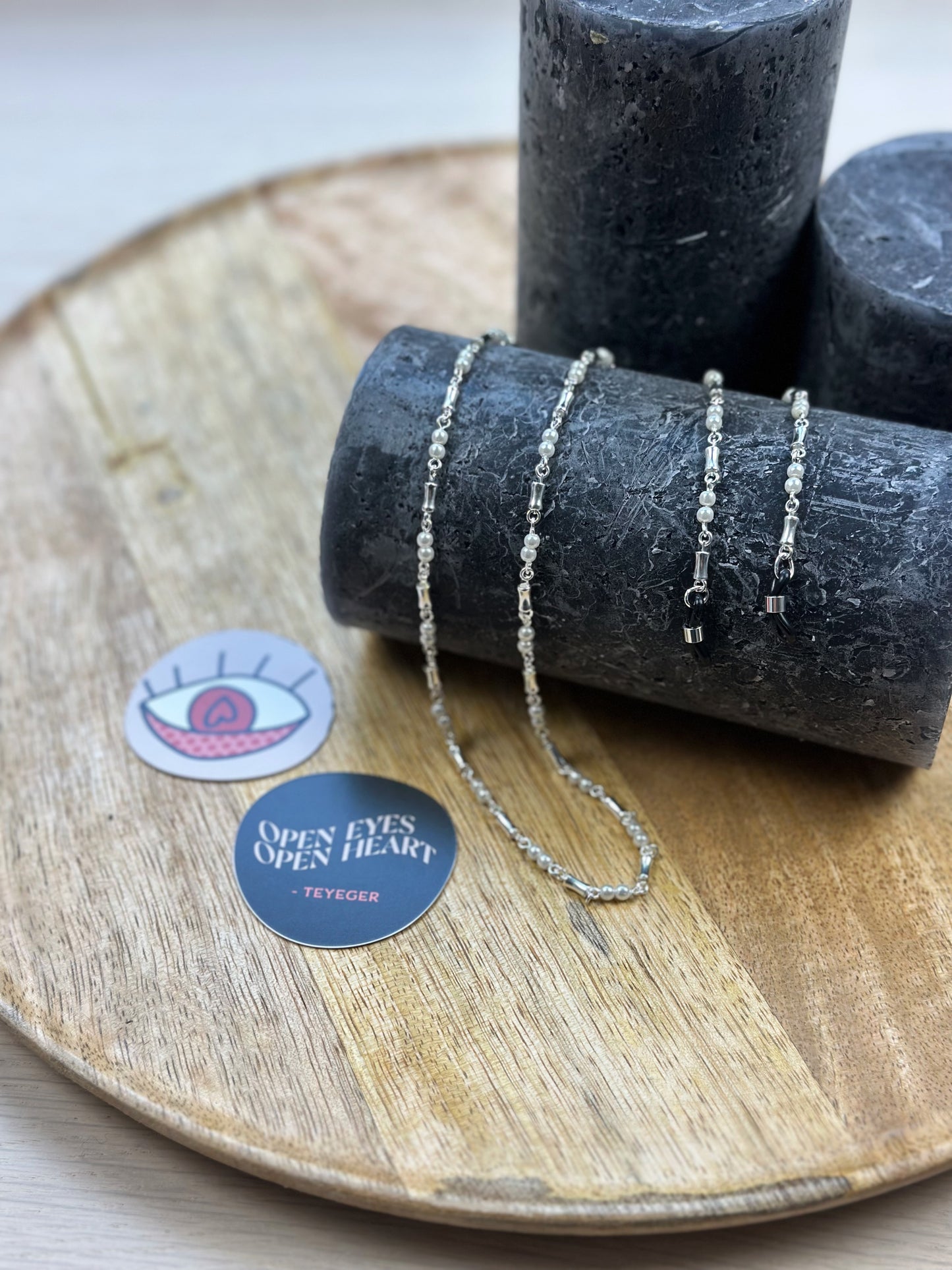 silberne Kette mit Perlen und Schmuckelementen ist über einen zylinderförmigen Gegenstand drapiert