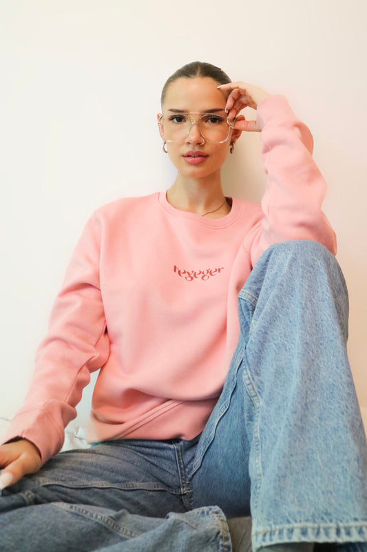 Frau mit Pilotenbrille blickt in die Kamera und trägt rosanen Pulli mit dem Aufdruck "Teyeger" auf Brusthöhe