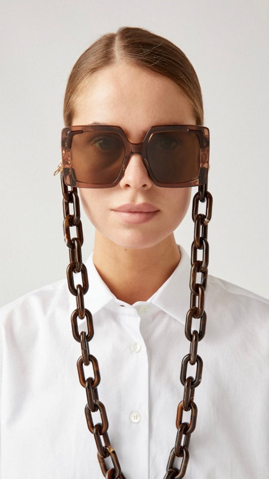 Frau trägt eckige, braune Sonnenbrille, an der eine Brillenkette bestehend aus großen braunen Kettengliedern, befestigt ist