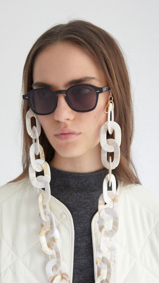 Frau trägt schwarze eckige Brille mit Brillenkette bestehend aus großen, perlmuttgemusterten, runden Gliedern
