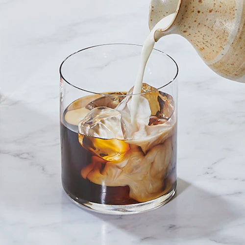 Milch wird in ein Glas mit Eiswürfeln, Kaffee und Kaffeeliqueur eingeschenkt