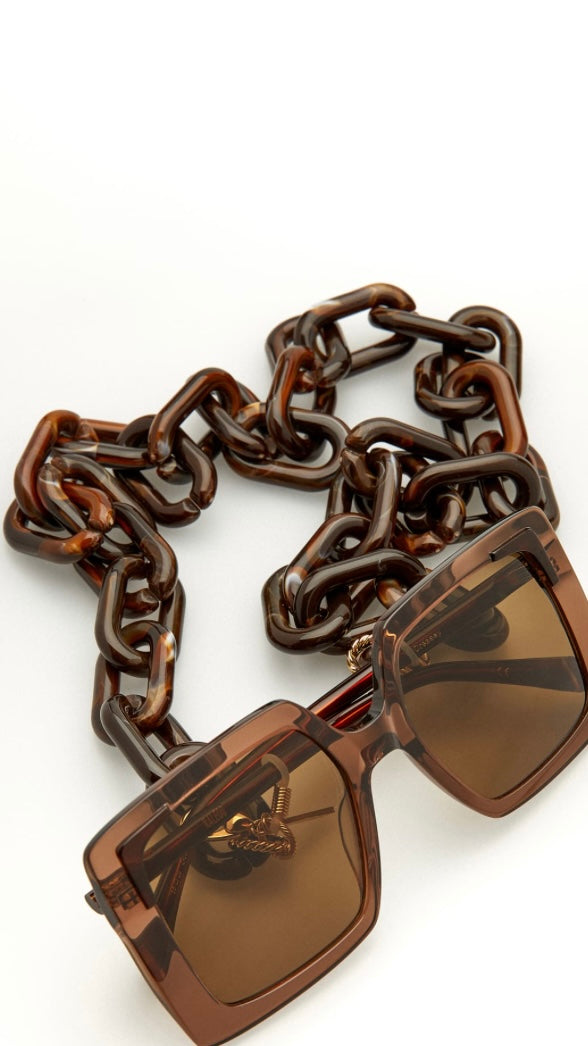 eckige, braune Sonnenbrille, an der eine Brillenkette bestehend aus großen braunen Kettengliedern, befestigt ist