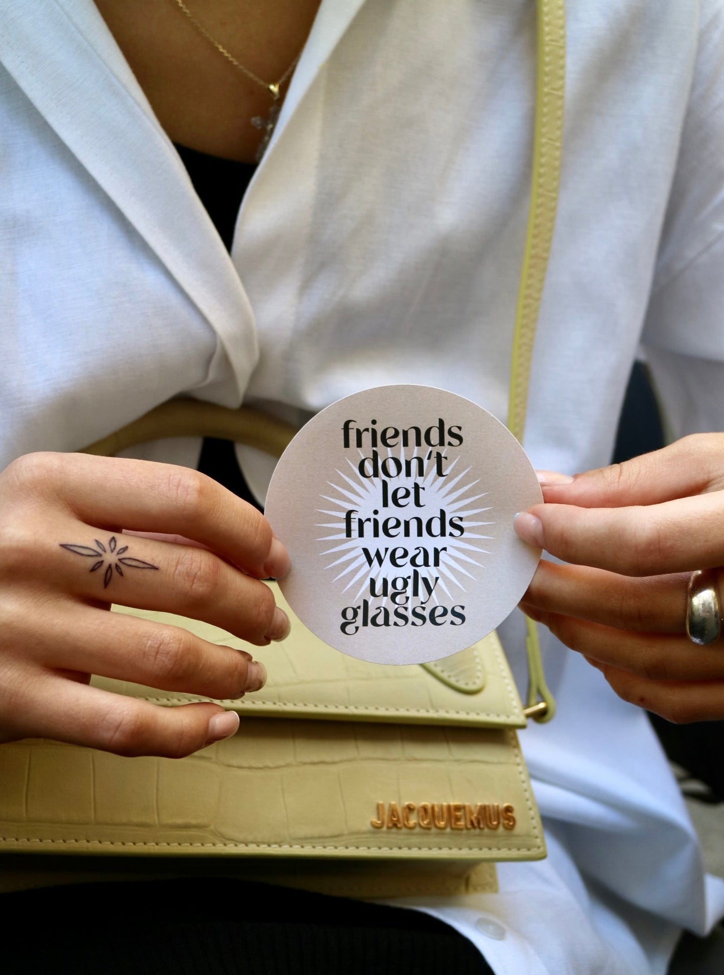 rundes, beigenes Sticker mit weißem sternförmigen Mittelteil und dem Aufdruck "Friends don't let friends wear ugly glasses"