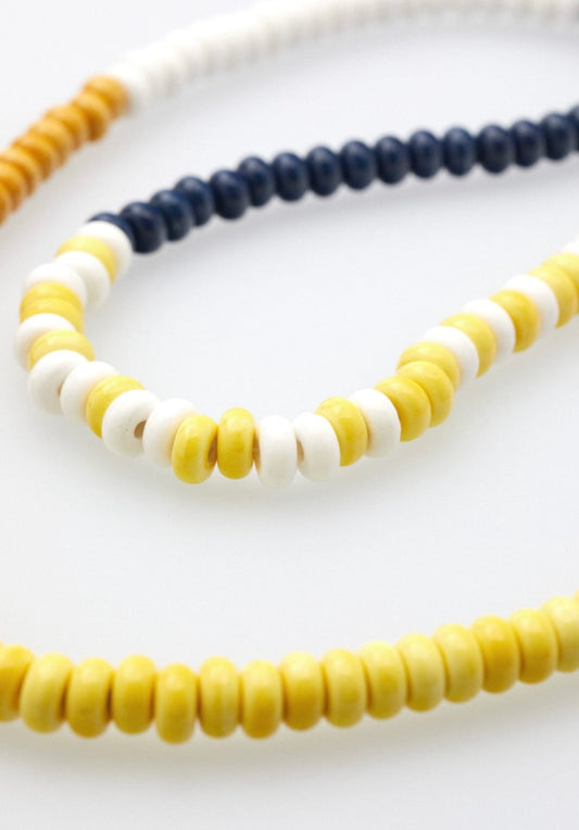 Nahaufnahme einer Brillenkette bestehend aus hellbraunen, weißen, dunkelblauen, gelben und rosanen Keramikperlen, die in einem Muster angeordnet sind