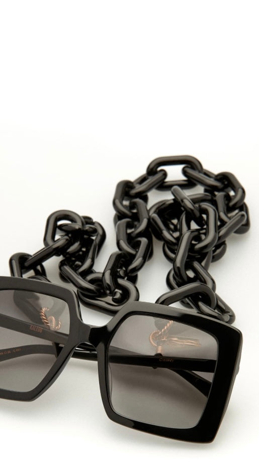 eckige, schwarze Sonnenbrille, an der eine Brillenkette bestehend aus großen schwarze Kettengliedern, befestigt ist