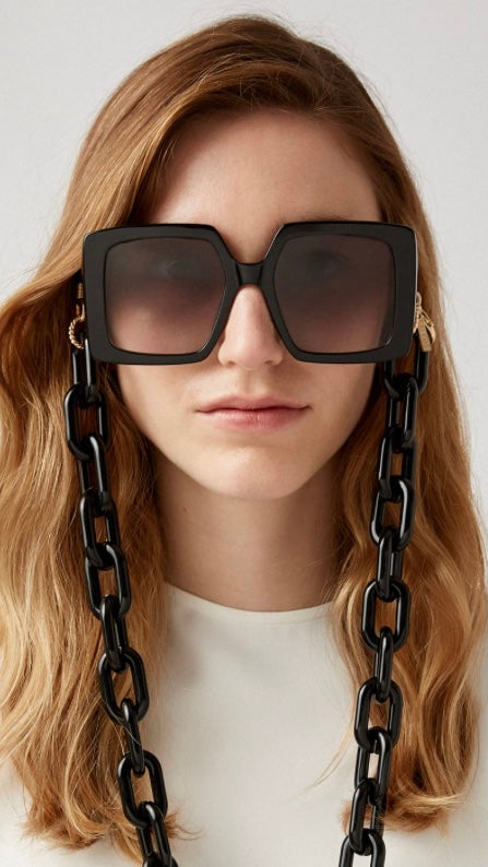 Frau trägt eckige, schwarze Sonnenbrille, an der eine Brillenkette bestehend aus großen schwarzen Kettengliedern, befestigt ist