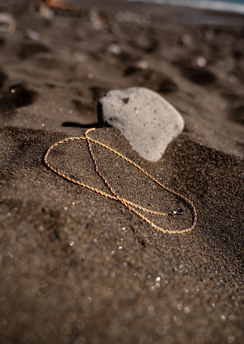 goldene, um sich selbst gedrehte Brillenkette liegt im Sand am Strand