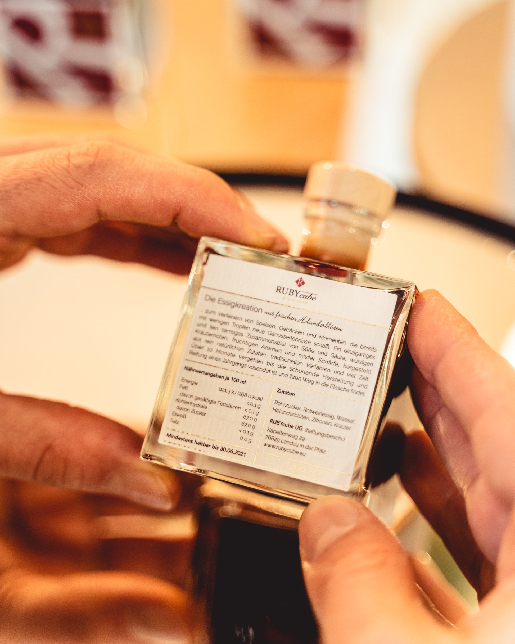 Rubycube Flasche wird in der Hand gehalten und von hinten auf dem Label die Inhaltsstoffe, Zutaten und Vision gezeigt