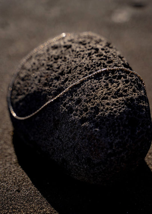 silberne Kette liegt auf Stein am Strand