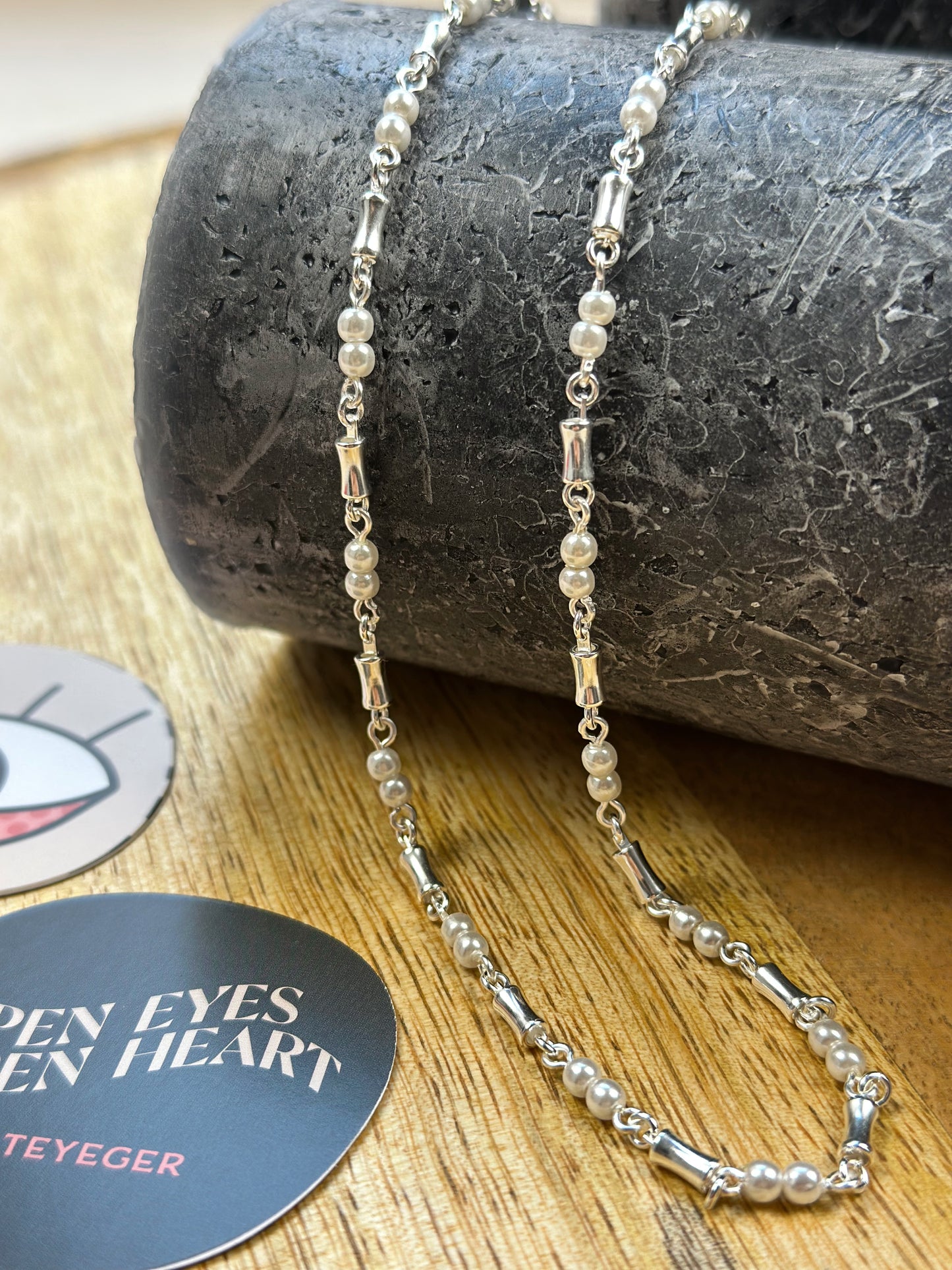 silberne Kette mit Perlen und Schmuckelementen ist über einen zylinderförmigen Gegenstand drapiert