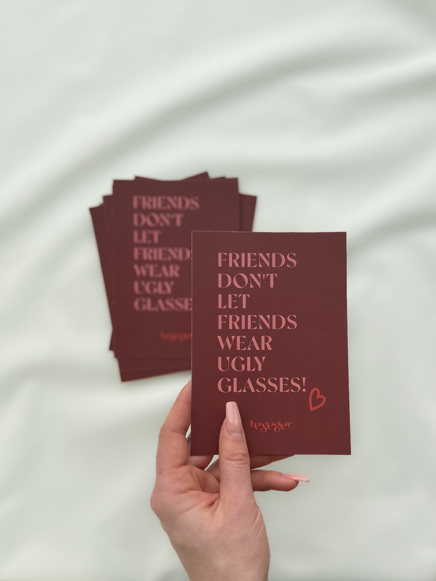 Eine Postkarte in der Hand mit "Friends don't let friends wear ugly glasses" Aufdruck