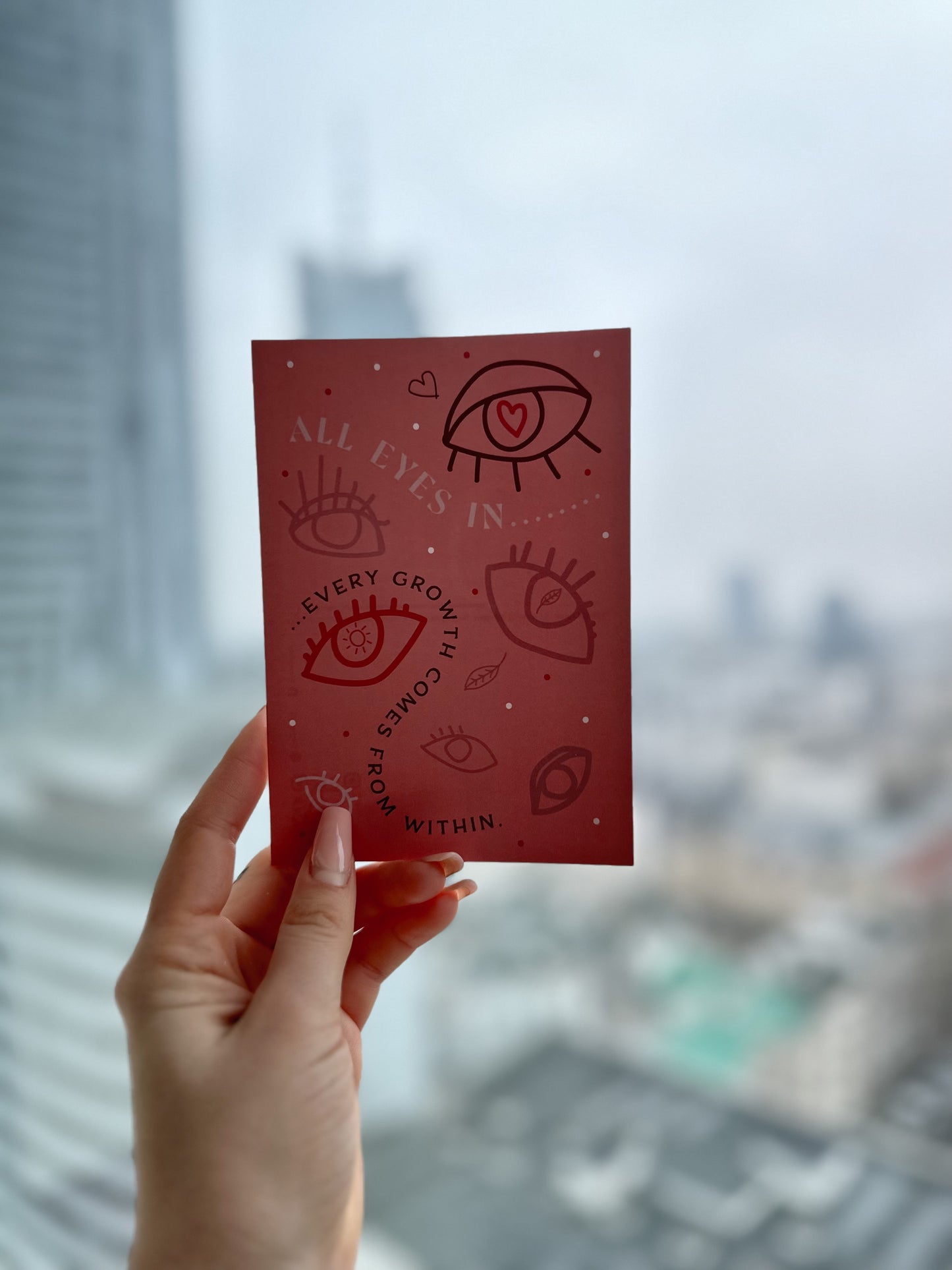 Eine Postkarte in der Hand vor ein Fenster gehalten mit Augen und "Every growth comes from within" Aufdruck