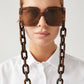 Frau trägt eckige, braune Sonnenbrille, an der eine Brillenkette bestehend aus großen braunen Kettengliedern, befestigt ist