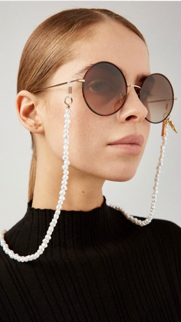 Frau trägt runde Sonnenbrille, an der Brillenkette aus perlmuttfarbenen Perlen befestigt ist 
