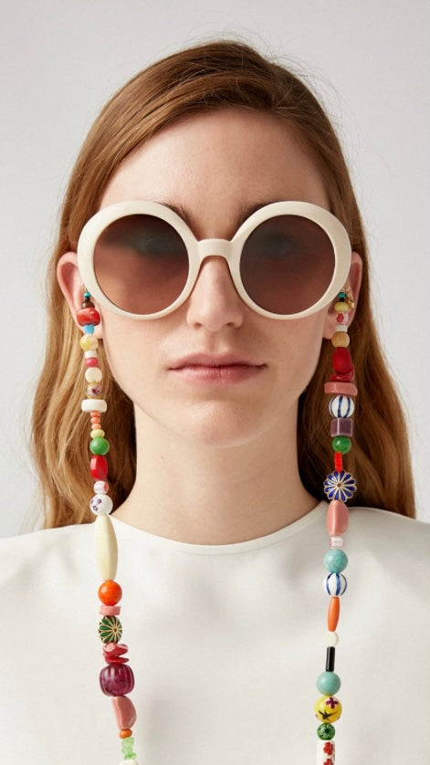 Frau trägt weiße, runde Sonnenbrille mit einer Brillenkette aus bunten Perlen