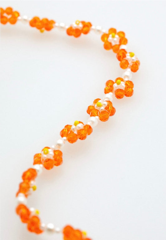 Nahaufnahme einer Brillenkette, die aus weißen, gelben und orangenen Perlen besteht, die jeweils als Blumen angeordnet sind