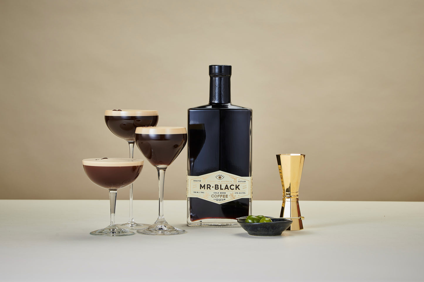 Flasche mit Mr. Black Coffee Liqueur Logo steht auf dem Tisch mit drei zubereiteten Espresso Martinis in unterschiedlich hohen Gläsern