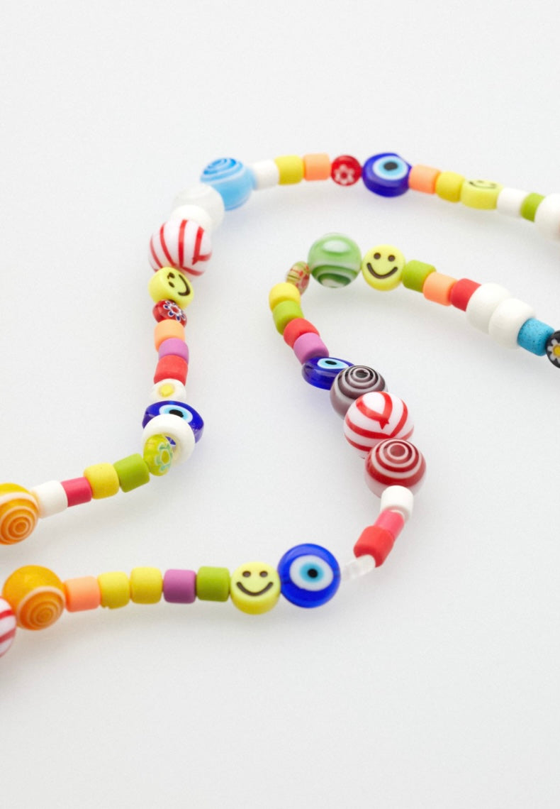 Nahaufnahme einer bunten Brillenkette mit Schmuckperlen. Die Schmuckperlen haben teilweise Muster, das sehende Auge oder Smileys aufgedruckt.