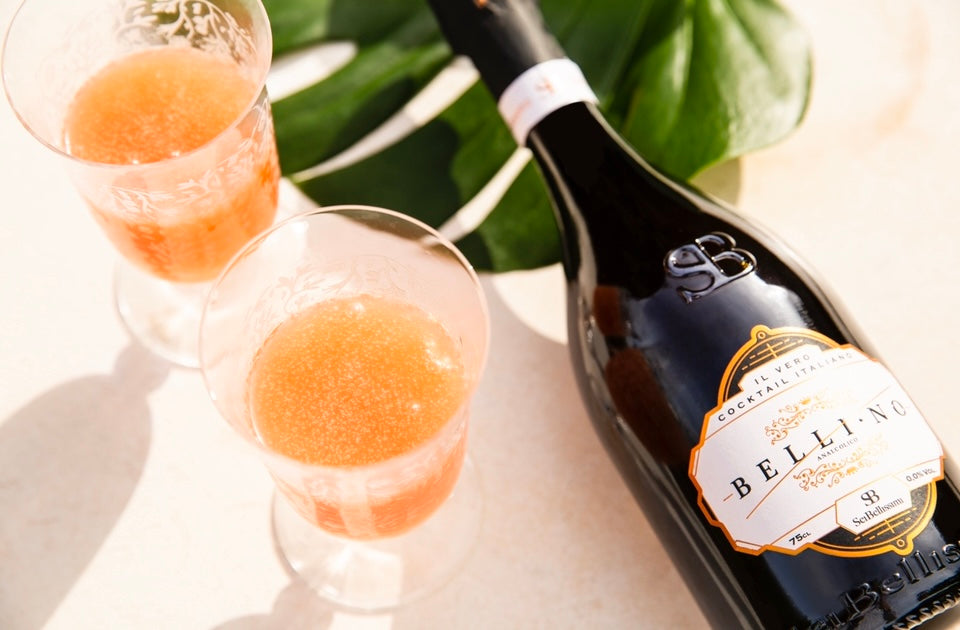 Zwei Gläser mit orangener Flüssigkeit und einer Belli-No Flasche liegen auf einem Tisch