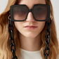 Frau trägt eckige, schwarze Sonnenbrille, an der eine Brillenkette bestehend aus großen schwarzen Kettengliedern, befestigt ist